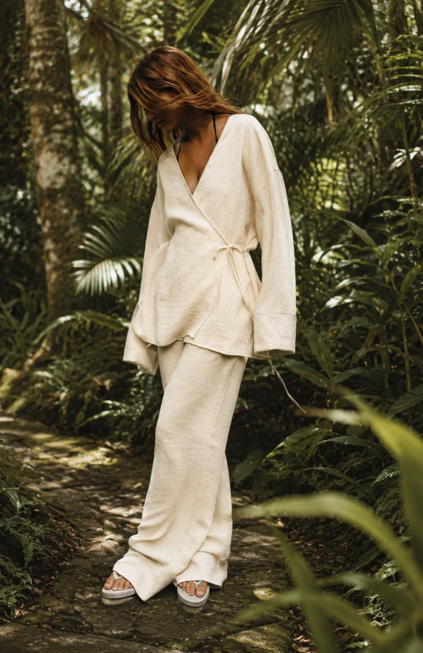 Woman in an unbleached linen kimono and wide trousers on a forest path